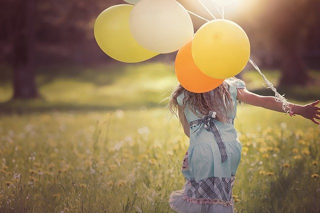 En pige med balloner løber på en græs eng